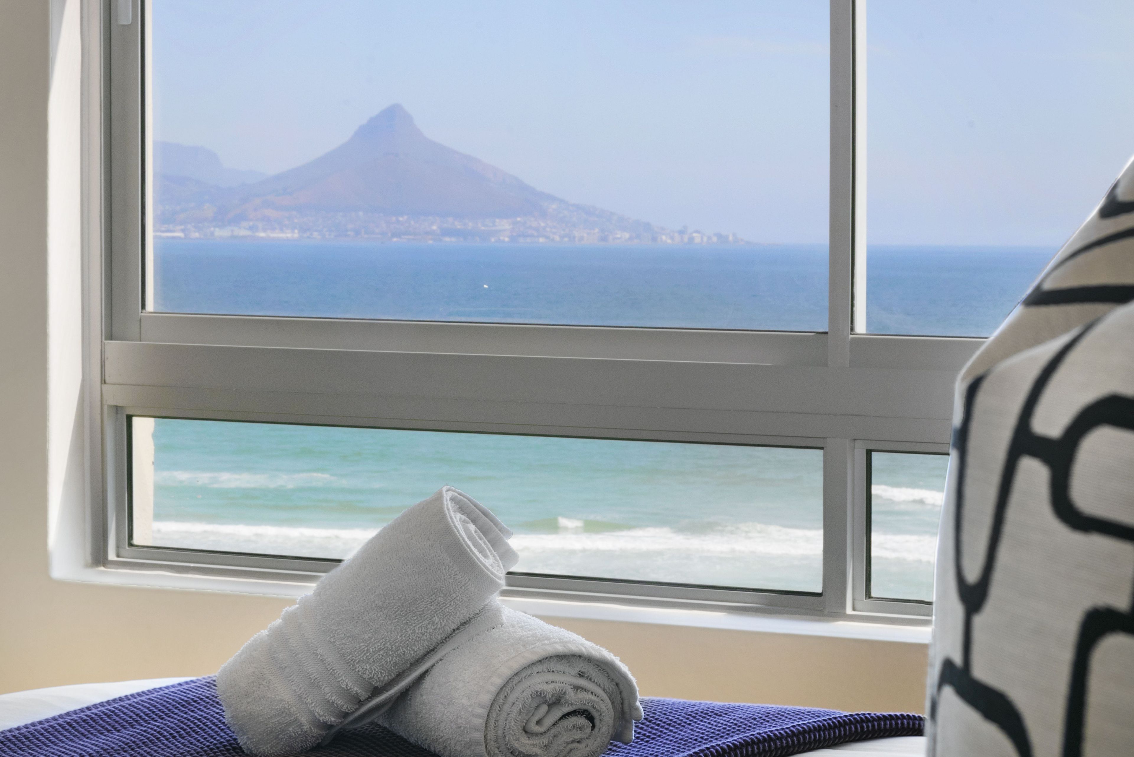 A room with a large window overlooking a coastal view, featuring a mountain and ocean.