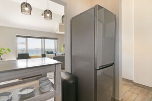 A modern kitchen with a large stainless steel refrigerator, a dining area with a view of the sea, and a minimalist design. - Sea Spray B404 by HostAgents (Cape Town)