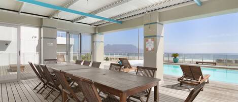A wooden deck with a pool, lounge chairs, and a table with chairs.