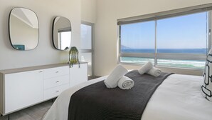 Ein modernes Schlafzimmer mit einem großen Bett, einer Kommode, zwei Spiegeln und Blick auf den Ozean.