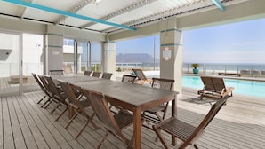 Eine Holzterrasse mit Pool, Liegestühlen und einem Tisch mit Stühlen.