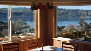 A dining area with a table and chairs, large windows with a view of a lake and surrounding landscape. - Cabañas Trayen Chiloé (Castro)