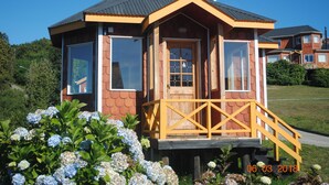 A wooden cabin with a balcony, large windows, and a chimney. - Cabañas Trayen Chiloé (Castro)