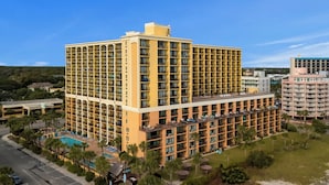 A multi-story hotel with balconies, a swimming pool, and a parking area.
