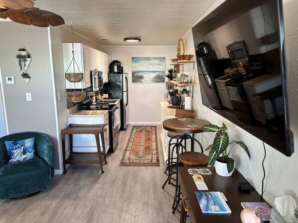 A compact kitchen with a dining area, a TV mounted on the wall, and a view of the outdoors.