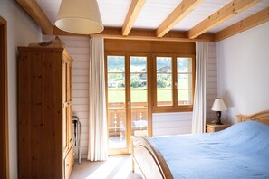Ein Schlafzimmer mit einem hölzernen Bett, einem Nachttisch mit Lampe, einem Holzschrank und einer Glastür, die auf einen Balkon führt.