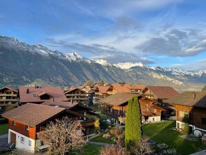 Ein Bergdorf mit traditionellen Holzhäusern, einem gepflegten Rasen und schneebedeckten Bergen im Hintergrund.