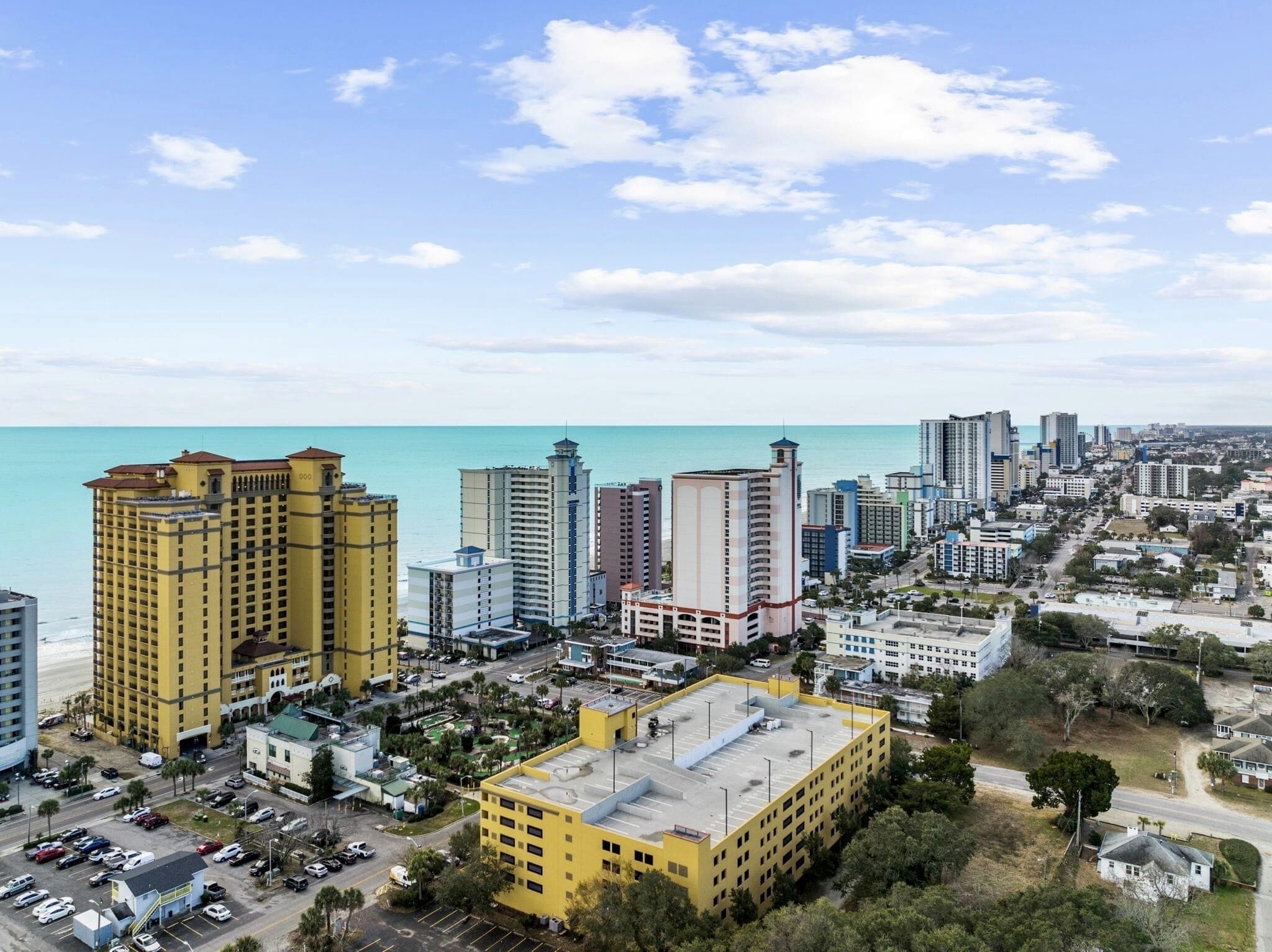 A coastal cityscape with high-rise buildings, a parking lot, and a clear view of the ocean.