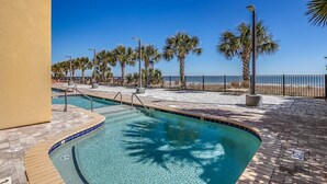 A pool area with clear blue water, palm trees, and a view of the beach.