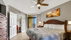 A bedroom with a bed, a ceiling fan, a painting, and a wooden dresser.