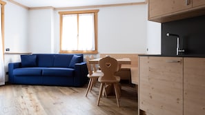 A compact living space with a blue sofa, wooden dining table, and a kitchenette. - Italianway - Castellazzi 12 Aquila (Bormio)