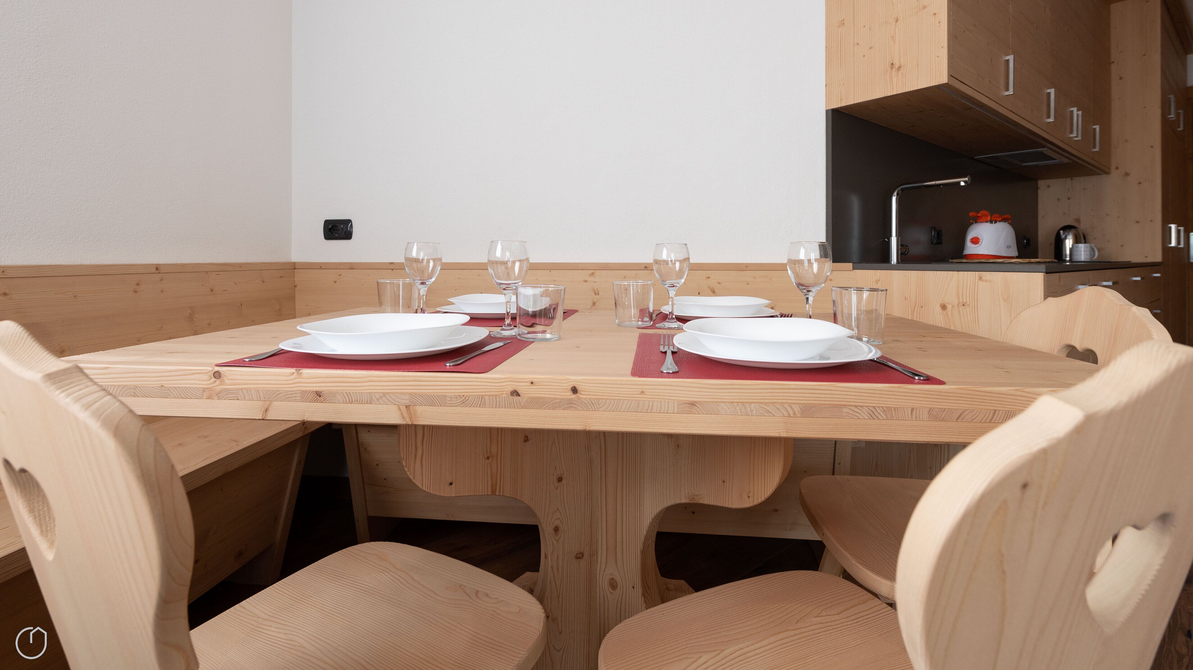 A wooden dining table set for four with red placemats, surrounded by wooden chairs.