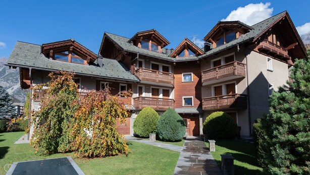 A multi-story chalet with wooden balconies and a stone pathway leading to the entrance. - Castellazzi 12 Aquila (Bormio)