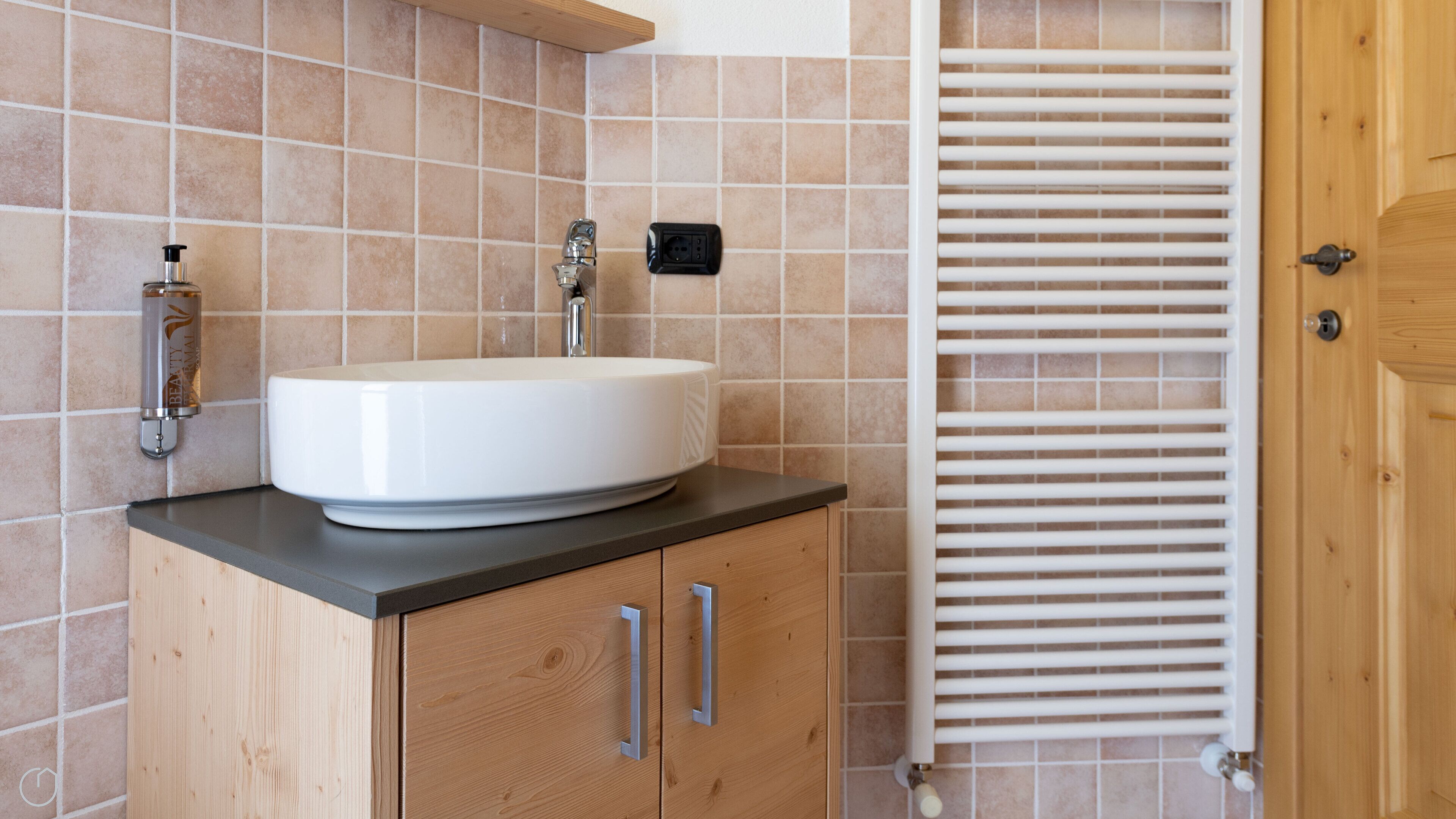 A bathroom with a white sink, wooden cabinets, a towel rack, and a wall-mounted heater.