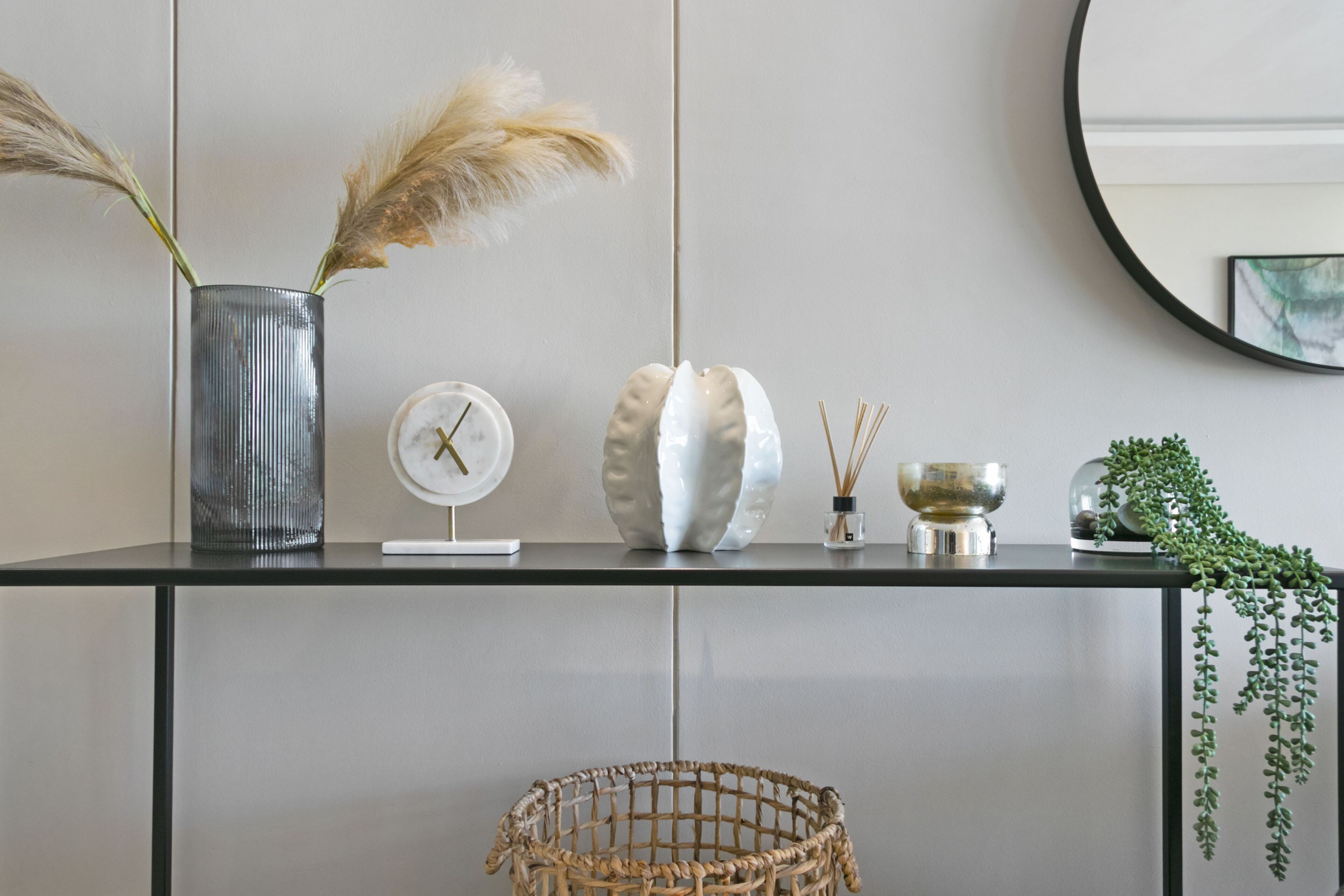 A modern interior with a glass table displaying decorative items, a woven basket, and a mirror on the wall.