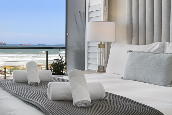 A hotel room with a bed, a view of the ocean, and a lamp.