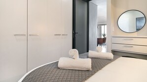 A modern hotel room with a bed, a round mirror, a wardrobe, and a door leading to another room.