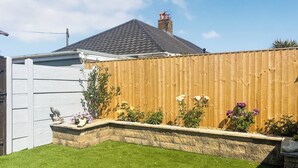 A backyard with artificial grass, a wooden fence, and various flowering plants.