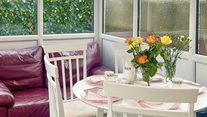 A cozy seating area with a white table set for two, featuring a vase with flowers, a teapot, and matching cups.