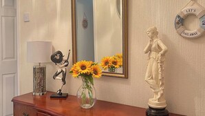 A wooden dresser with a mirror, a statue, a figurine, and a vase with sunflowers.