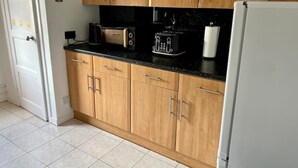 A kitchen with wooden cabinets, a black countertop, and a white refrigerator. - Charming Seaside home. sleeps 4 with free parking (Dundee)