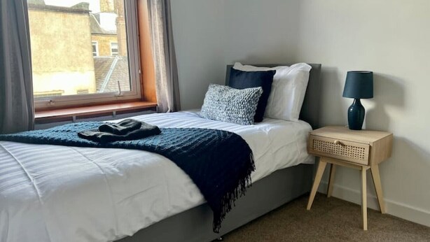 A bedroom with a bed, a bedside table, a lamp, and a window. - Charming Seaside home. sleeps 4 with free parking (Dundee)