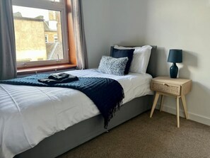 Une chambre à coucher avec un lit, une table de chevet, une lampe et une fenêtre.