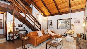 A cozy living room with a wooden staircase, a brown leather sofa, a coffee table, and a hanging chair. - Closer to the Stars Fire Pit Dog-Friendly (Big Bear Lake)