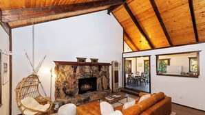 A cozy living room with a stone fireplace, a hanging chair, and a leather sofa. - Closer to the Stars Fire Pit Dog-Friendly (Big Bear Lake)