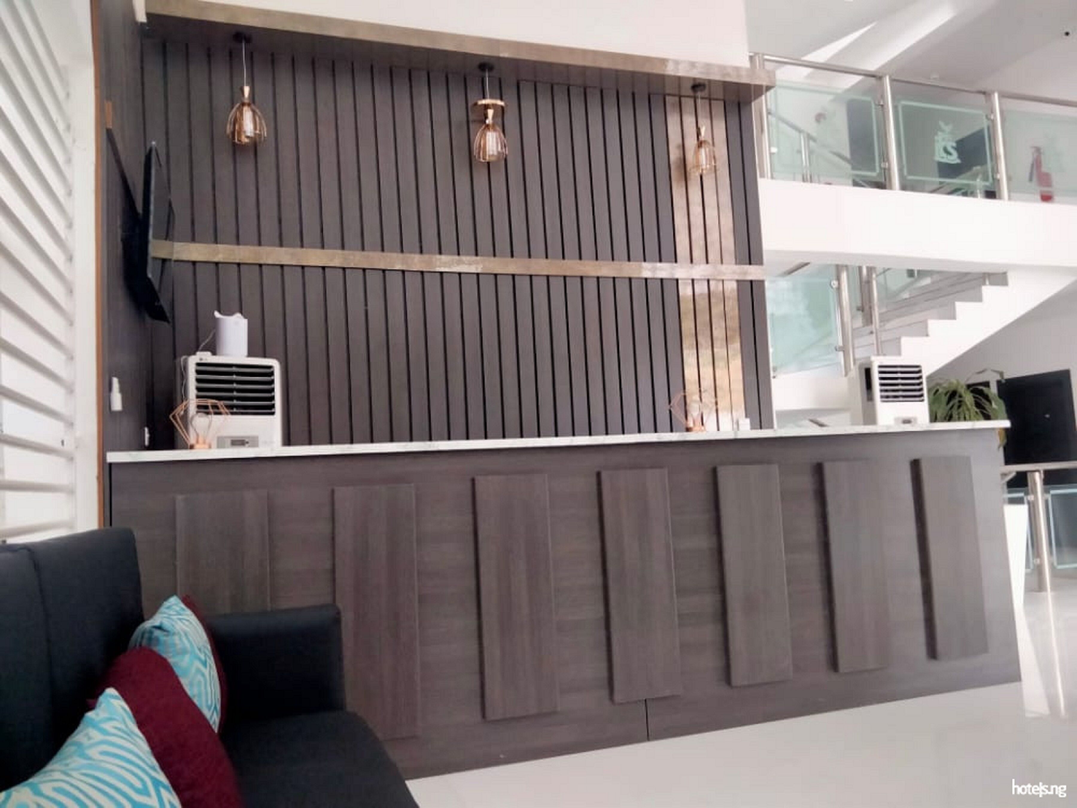 A modern hotel reception area with a dark wood panel wall, two pendant lights, and a white counter.