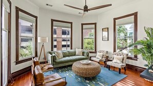 Ein geräumiges Wohnzimmer mit einem grünen Sofa, zwei Sesseln, einem runden Couchtisch und einem Deckenventilator.