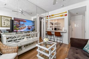 Een moderne woonkamer met een televisie, een witte tv-kast, een eethoek met twee stoelen, en een keuken.
