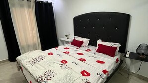 Un dormitorio con cama, mesita de noche, lámpara y ventana con cortinas.
