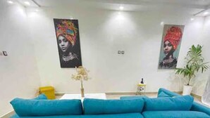 Un salón moderno con un sofá azul, dos obras de arte colgadas en la pared, una mesita con un florero y una planta en maceta.