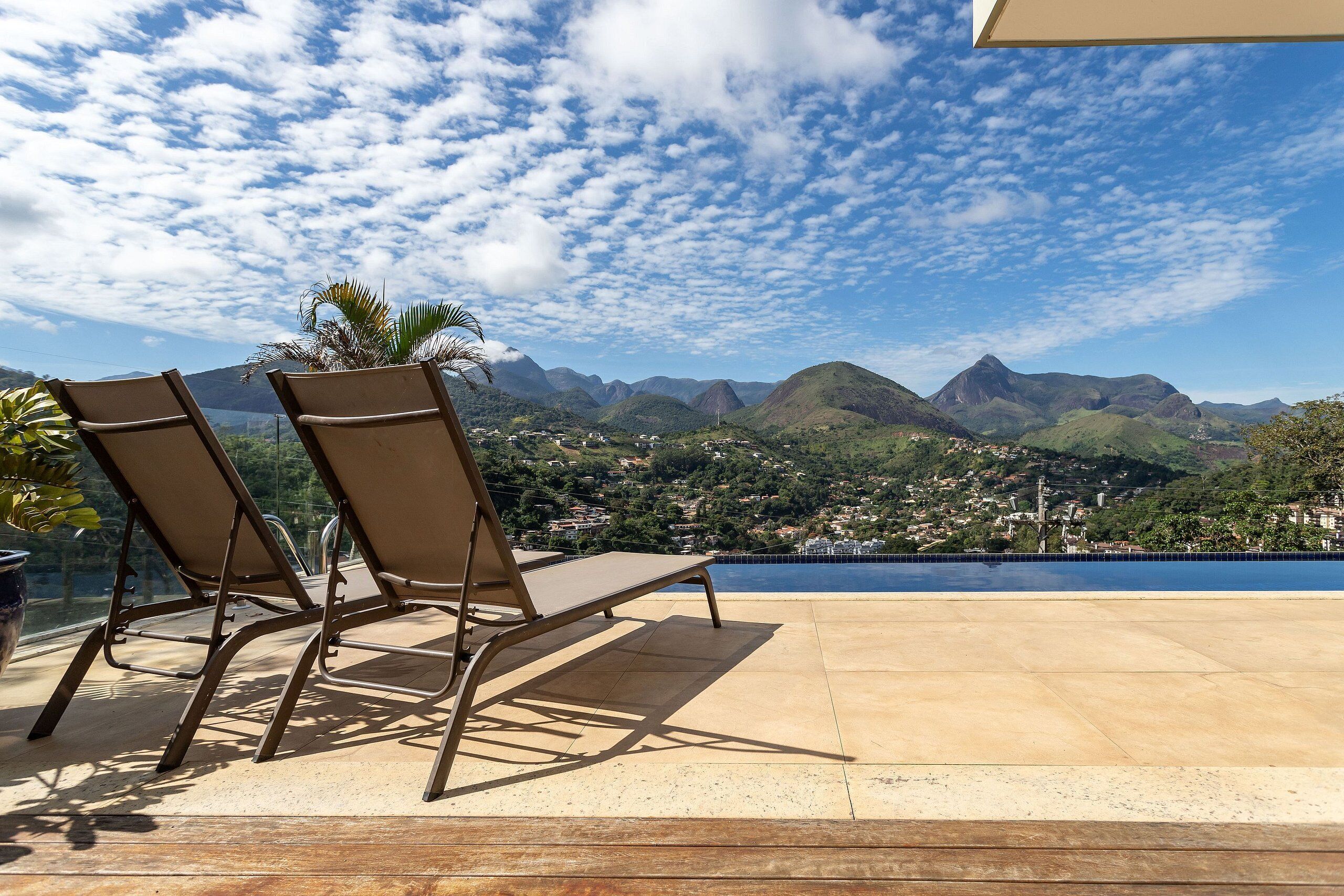 A terrace with two lounge chairs and a view of mountains and a town.