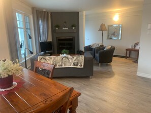 Ein Wohnzimmer mit Kamin, einer Couch, einem Esstisch mit Stühlen und einem Fernseher.