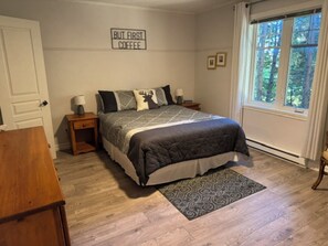 Een slaapkamer met een bed, nachtkastjes, een vloerkleed, een raam met gordijnen en een bord aan de muur.