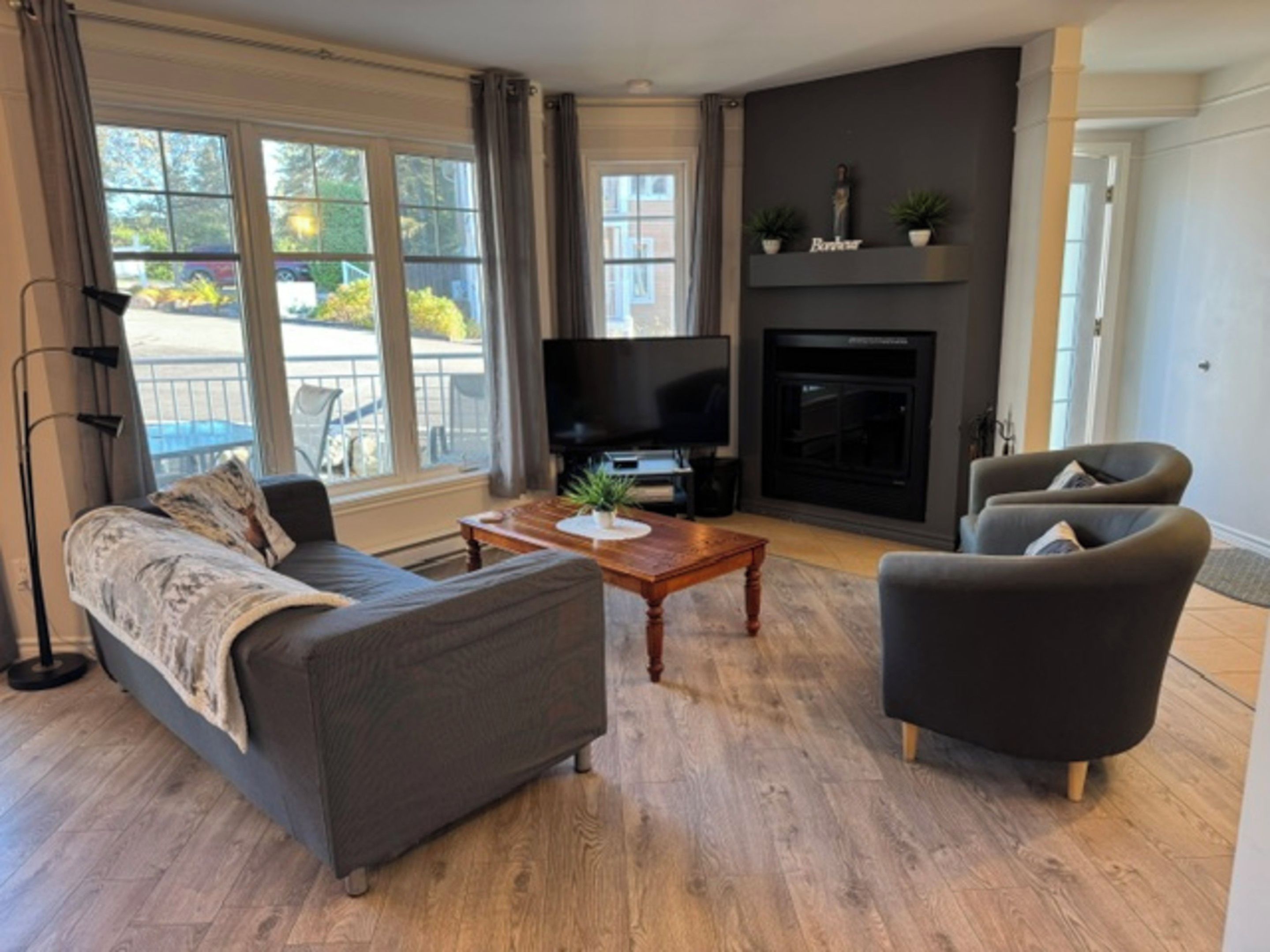 Un salon moderne comprenant un canapé, un fauteuil, une table basse, un téléviseur, une cheminée et de grandes fenêtres.