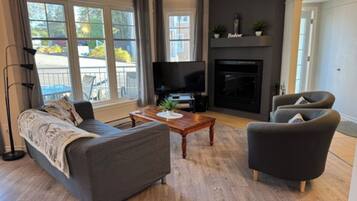Un salon moderne comprenant un canapé, un fauteuil, une table basse, un téléviseur, une cheminée et de grandes fenêtres.