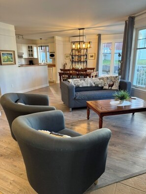 Un salon comprenant un canapé, deux fauteuils, une table basse et un coin repas agrémenté d’un lustre.