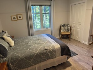 A bedroom with a bed, a window, a chair, and a door. - Lake Archambault, Apartment 316 (Saint-Donat-de-Montcalm)