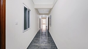 A long, narrow hallway with white walls and a dark marble floor. - Treebo SLN Heritage (Bengaluru)