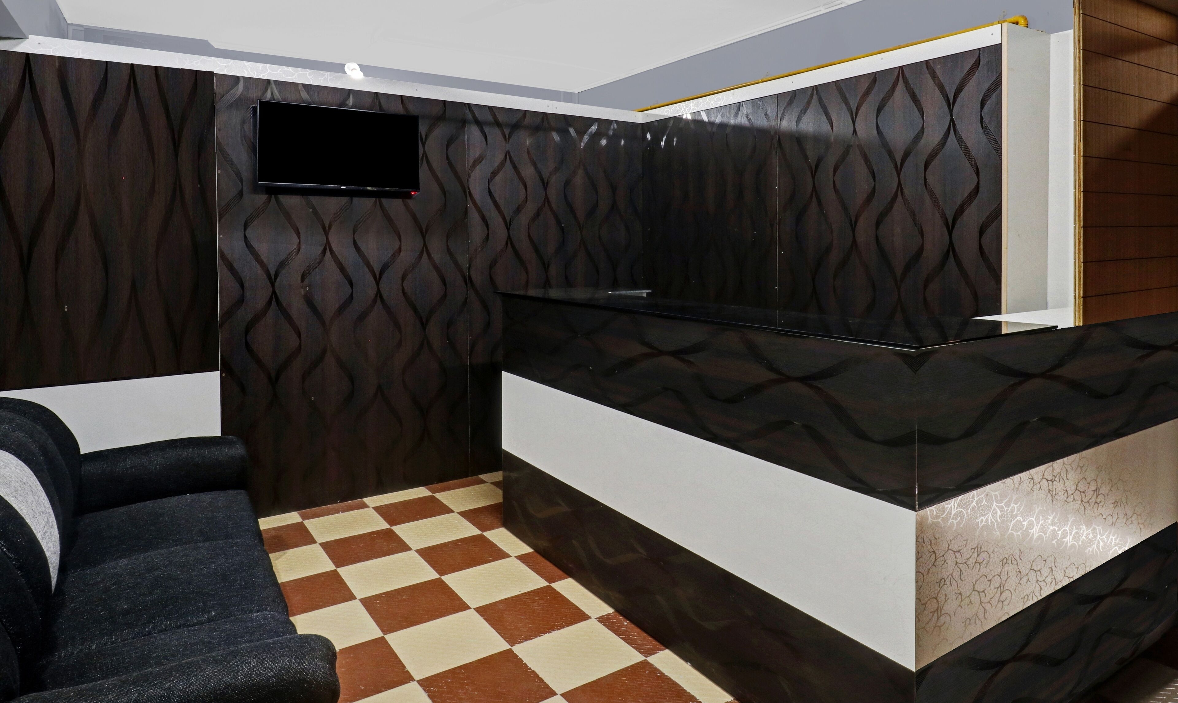 Una habitación de hotel moderna con suelo a cuadros, un sofá, un televisor de pantalla plana en la pared y un mostrador de recepción.