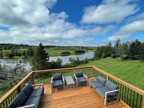 Eine Terrasse mit Gartenmöbeln mit Blick auf einen See und viel Grün.