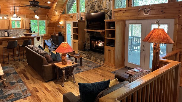 A spacious cabin interior with a stone wall, wooden ceiling, a fireplace, and a dining area. - River Shoals Cabin! Hot Tub-Water front (Cleveland)