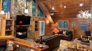 A cozy cabin interior with a stone fireplace, wooden ceiling, and large windows. - River Shoals Cabin! Hot Tub-Water front (Cleveland)