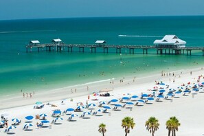 A beach with a pier and beach umbrellas.