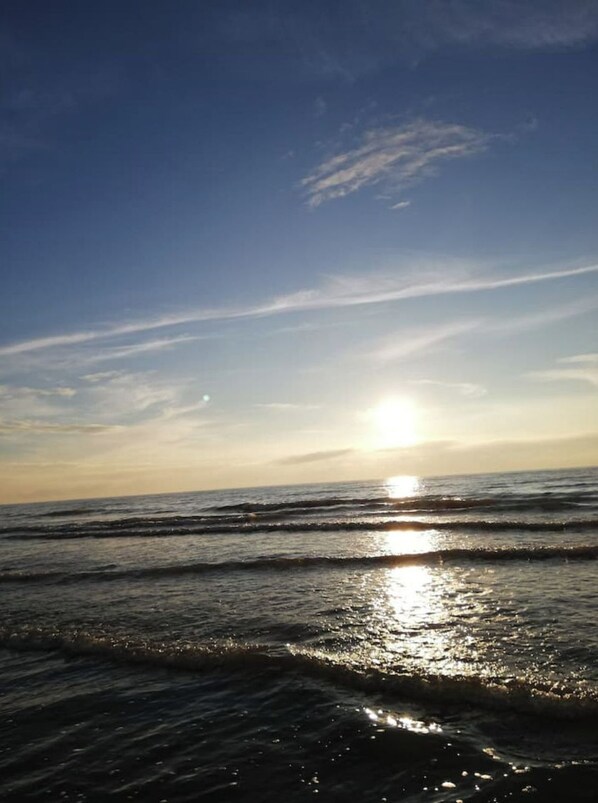 Une scène de plage où le soleil se couche sur l’océan, créant une atmosphère paisible et sereine.