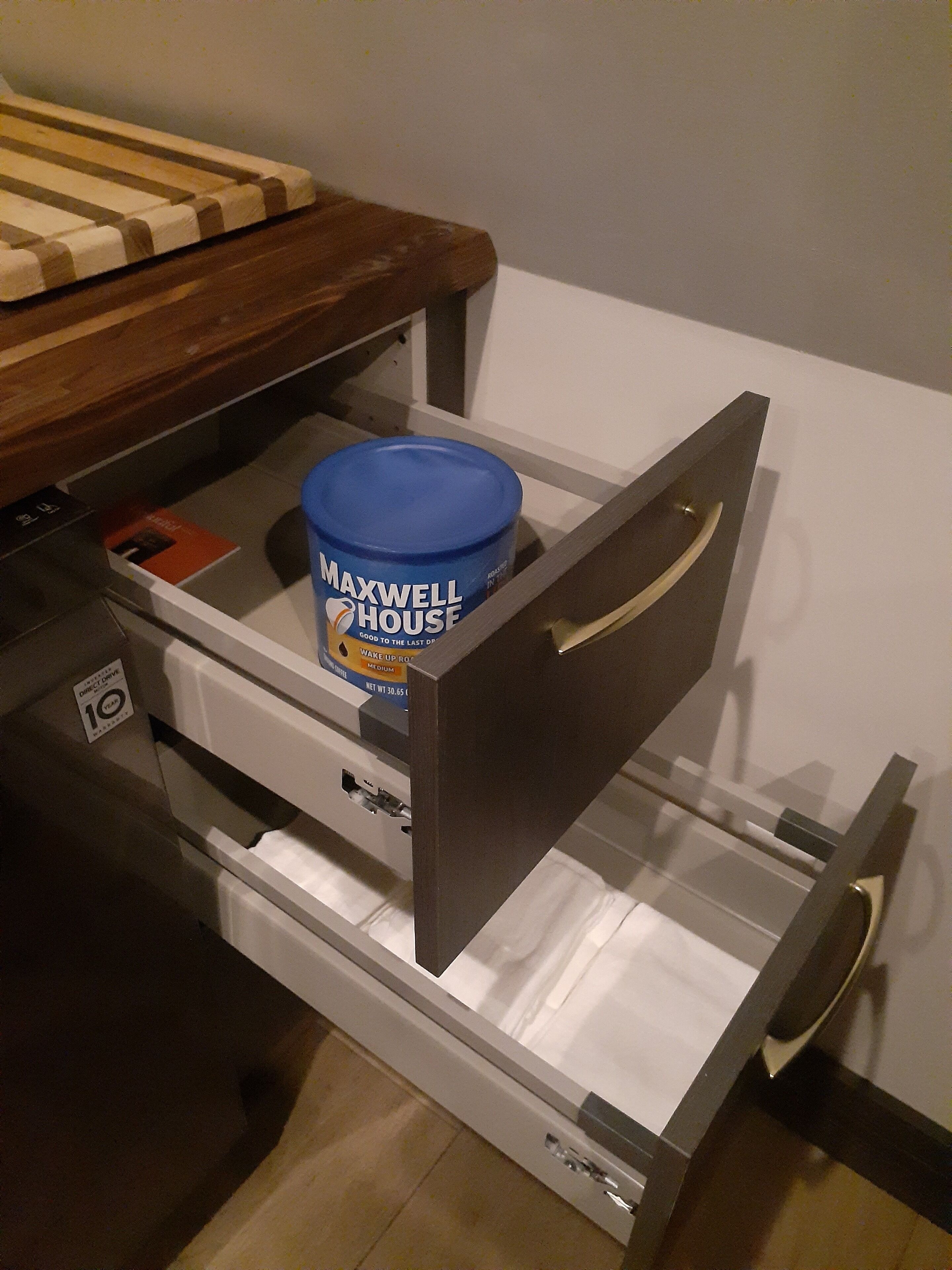 A drawer with a blue container labeled "Maxwell House" and a wooden bed frame above it.