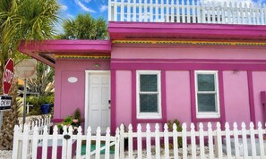 A pink building with a white picket fence, a stop sign, and a one-way sign.